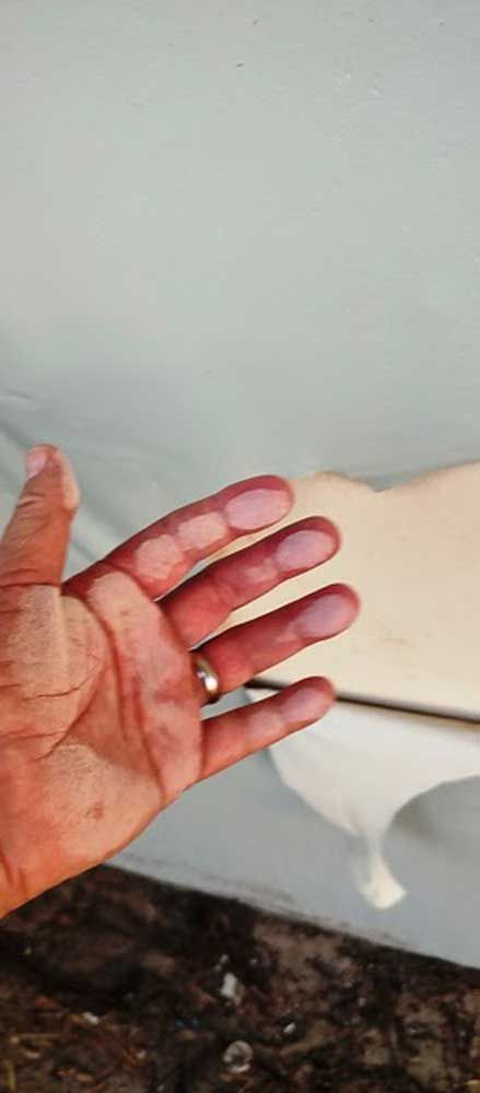 Open hand with red-stained palm held in front of a white wall and dark floor.