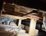 Copper plumbing pipes and electrical wiring run between wooden floor joists in a dark crawl space.