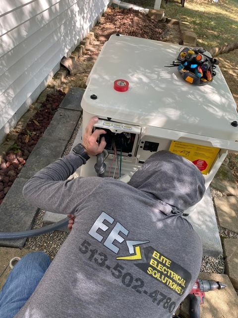 A tan residential standby generator sits on a concrete pad next to a white wooden deck and a grassy lawn.