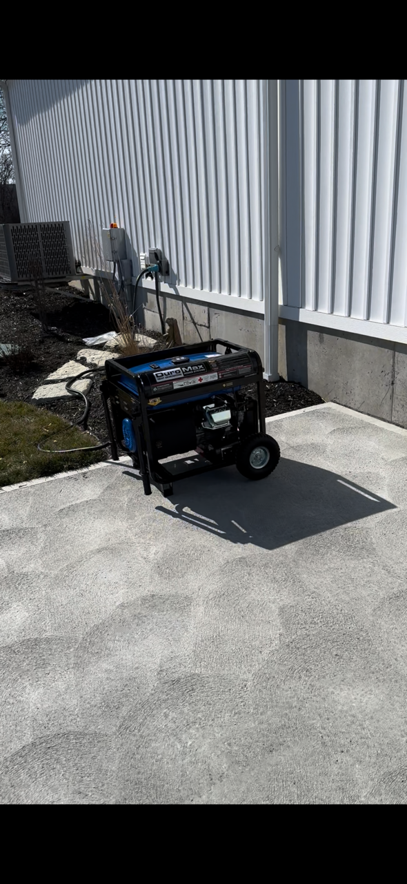 Small black wheeled machine on a concrete path beside a striped fence in bright sunlight