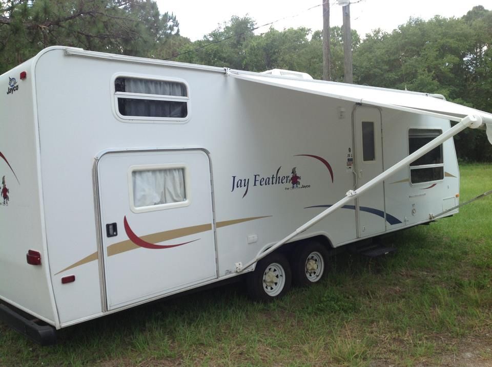 White RV with An Awning Is Parked in A Grassy Field