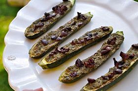 Grilled zucchini halves topped with chopped herbs and bits of bacon on a white plate