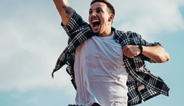 Cheering person in a plaid shirt with arms raised against a bright sky
