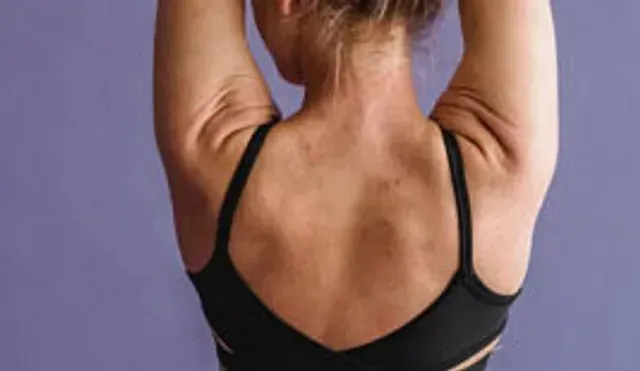 Back view of a person in a black sports bra stretching with arms raised overhead