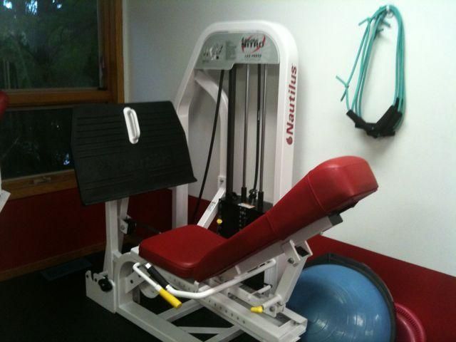 Red and white leg press machine in a gym, with a black weight stack and blue stability ball nearby