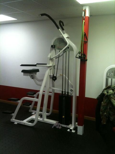 White gym pull-up and dip machine beside a red wall-mounted strap in a fitness room