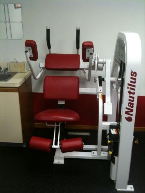 Red Nautilus workout machine with padded seat in a gym or clinic room