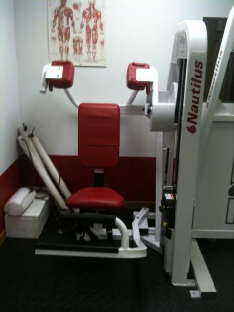 Red and white Nautilus exercise machine in a gym room with anatomical poster on the wall