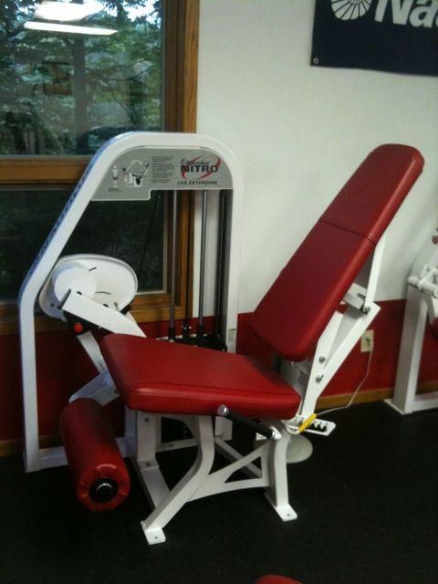 Red and white exercise machine with padded seat and backrest in a gym or rehab room