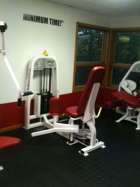 Gym room with red and white exercise machines and wall text reading “MINIMUM TIME”