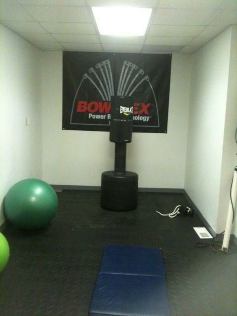 Small fitness room with a punching bag, exercise balls, mats, and a banner on the wall.