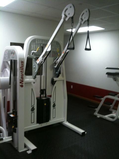 Gym cable exercise machine in a mirrored room with dark flooring and red wall accents.