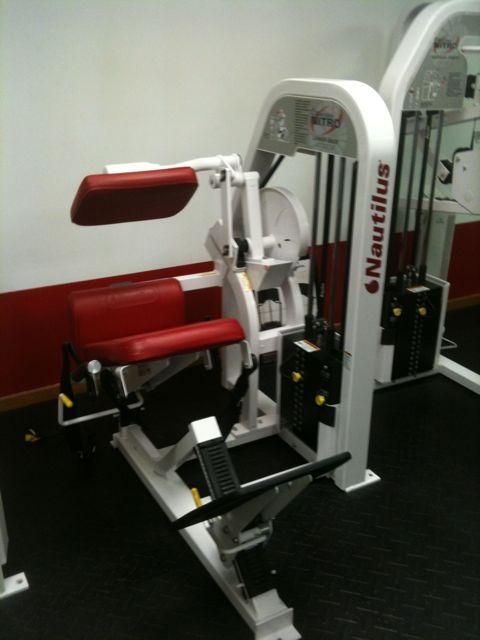 Red Nautilus exercise machine with padded seat and arm pads in a gym.