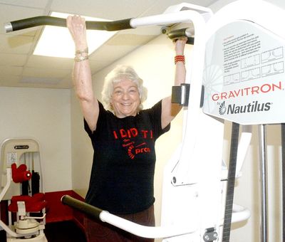 Smiling woman using a Nautilus Gravitron exercise machine in a gym, wearing a black T-shirt.