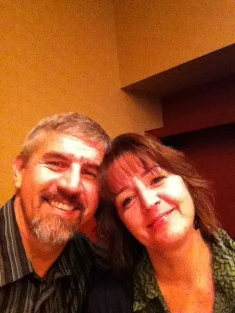 Two smiling people posing closely together in warm indoor lighting.
