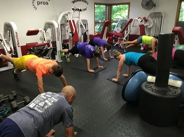 People doing plank exercises in a gym studio with exercise balls and machines.