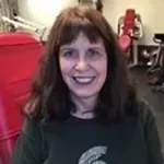 Janet Murphy smiling in a red chair, with dark hair and a blurred gym background