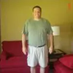 Person standing in a room between red couches, wearing a green shirt and light shorts.
