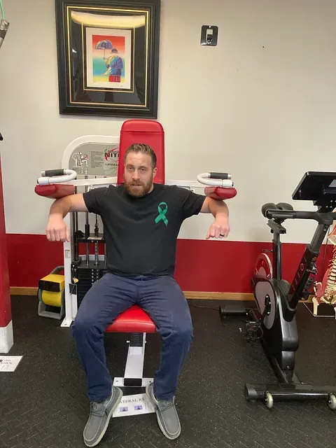 Man sitting on a red exercise machine in a gym, with stationary bikes beside him.