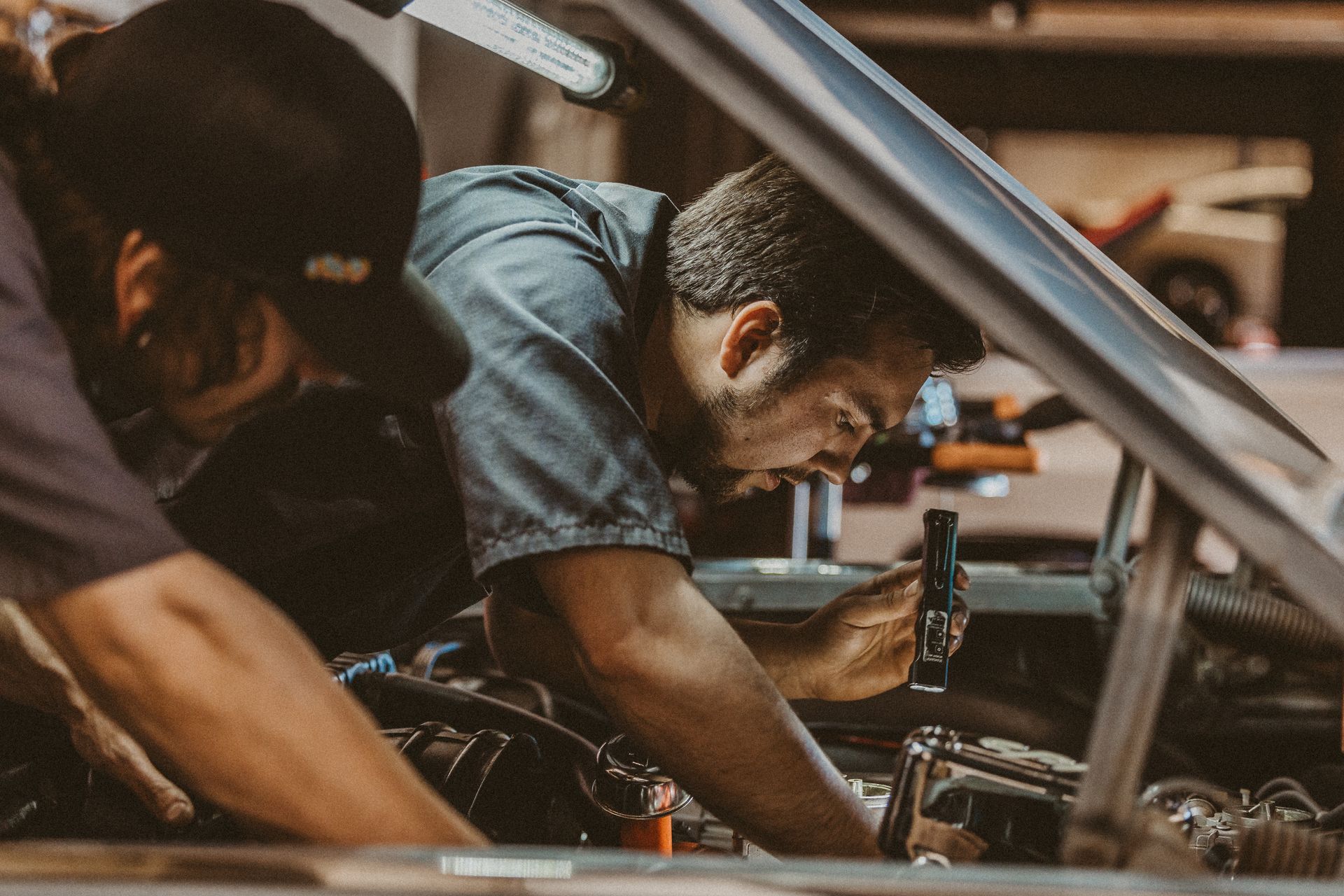 Two mechanics working under a car hood in a garage, focused on engine repairs.