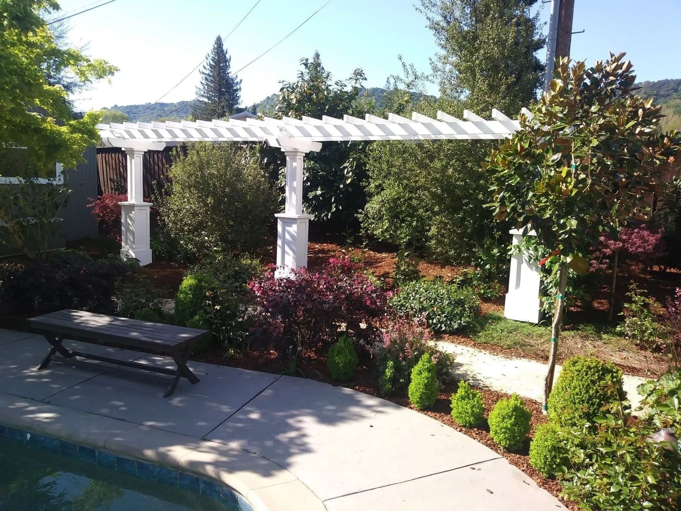 A white pergola over a swimming pool in a garden
