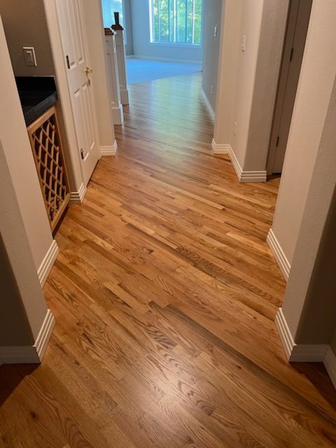 Wooden hallway floor with a glossy finish leading to a bright room at the end