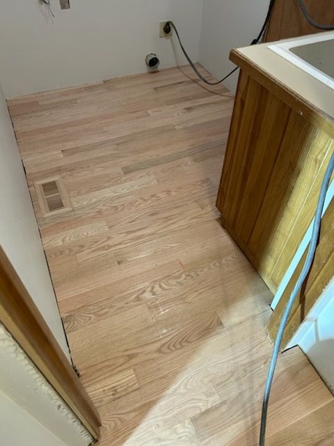 Partially renovated kitchen with bare wood floor, cabinet on the right, and exposed cords along the wall