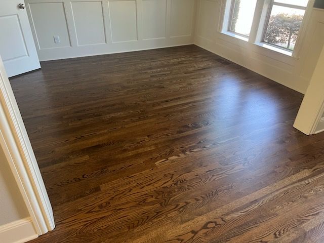 Empty room with dark hardwood floors, white walls, and large windows letting in sunlight