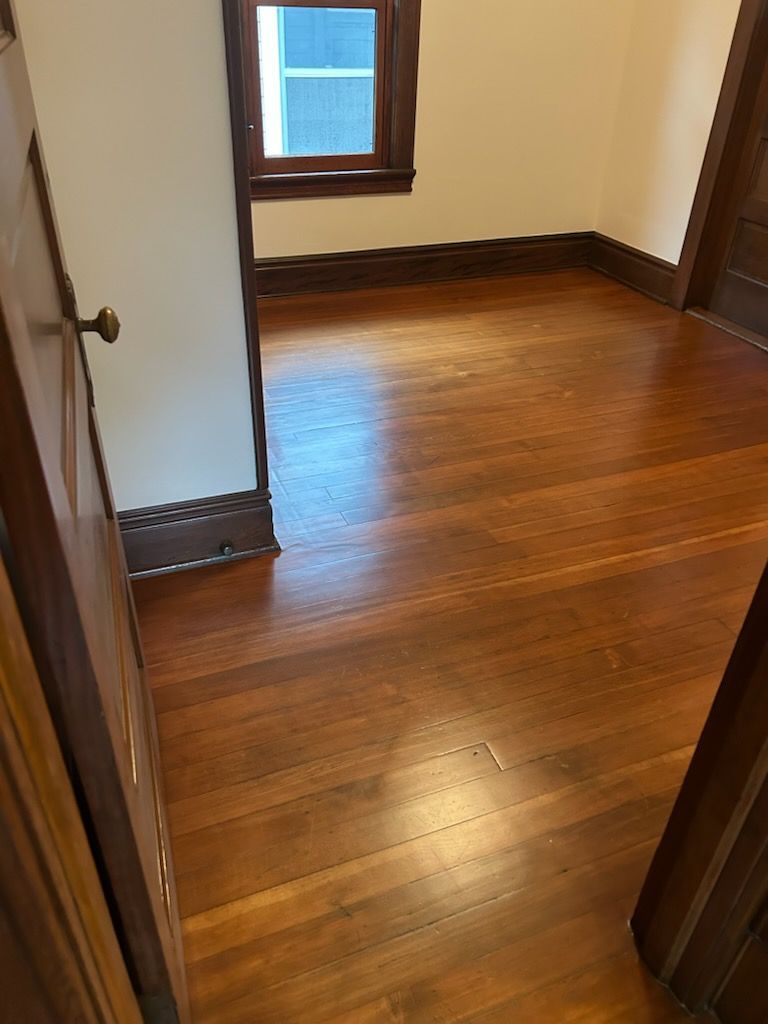 Empty hardwood-floored room with a small window and dark wood trim