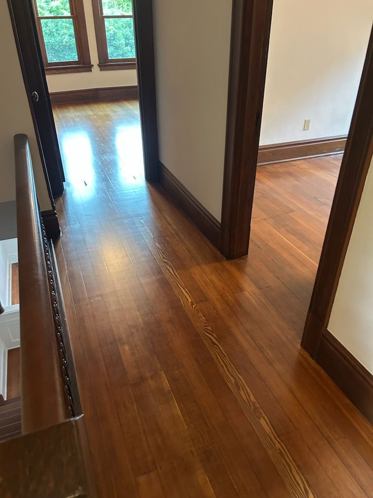 Wooden hallway with glossy floors, white walls, dark trim, and sunlight from a windowed doorway.