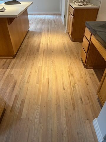 Empty kitchen with light wood floor and cabinets, viewed down a central walkway.