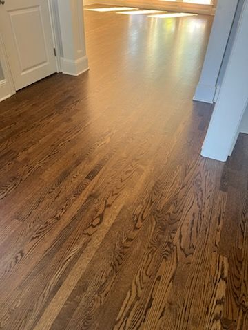 Wooden hallway floor with sunlight streaming in from a bright room ahead
