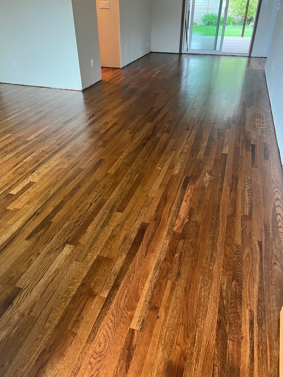 Empty room with glossy dark wood floors and sliding glass doors at the far end