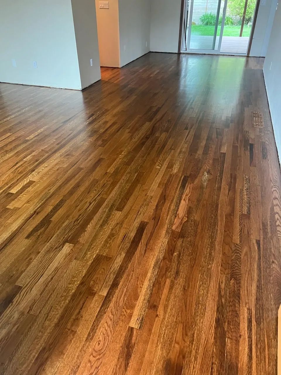 Empty room with polished dark wood floors and sliding glass doors at the far end.