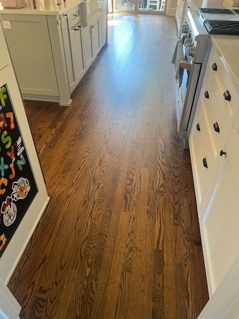 Kitchen hallway with wood flooring, white cabinets, and an open refrigerator on the left.