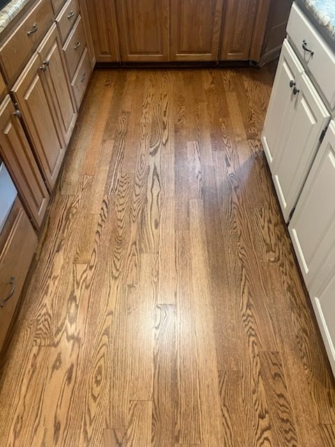 Wooden kitchen floor between wood and white cabinets, with sunlight reflections.
