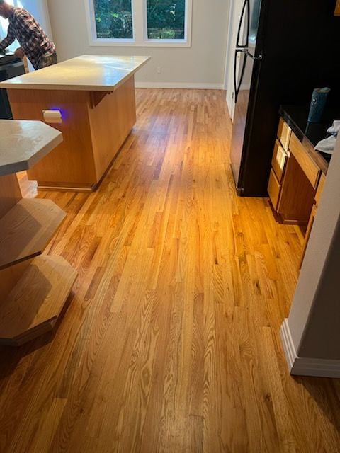 Wooden kitchen with island, hardwood floor, window, and black refrigerator.
