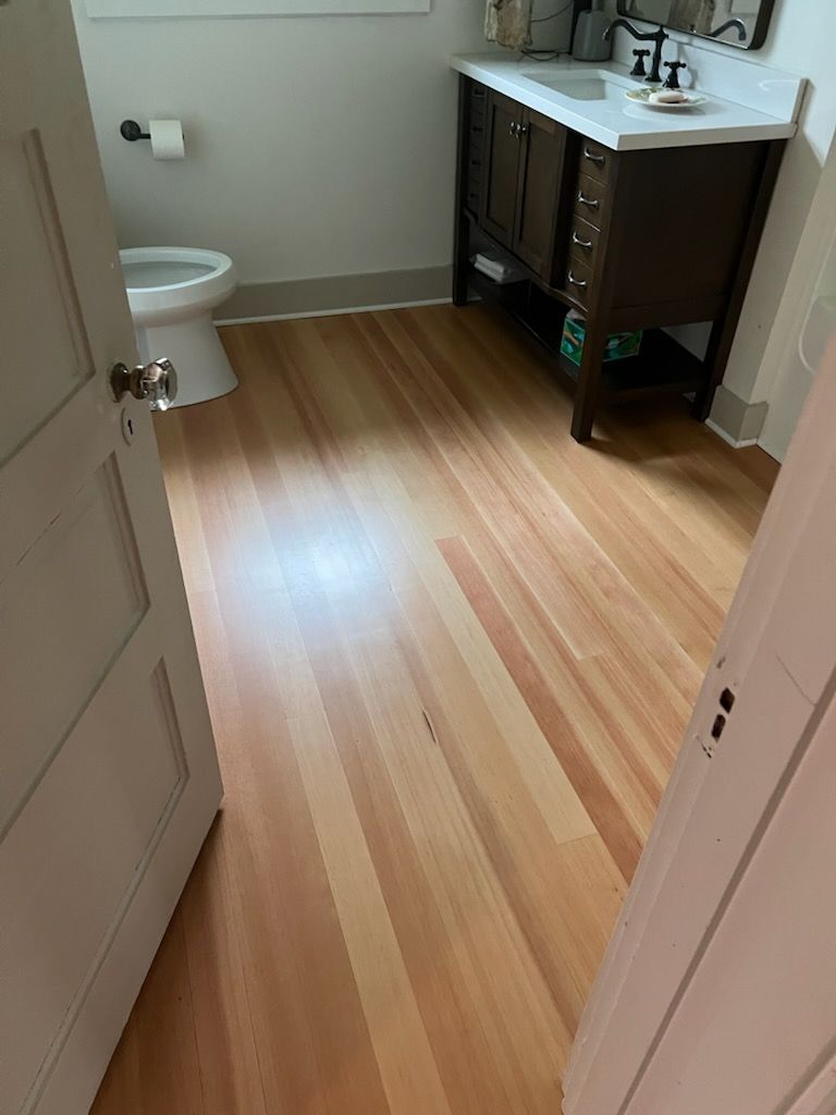 Small bathroom with wood floor, white toilet, and dark vanity with sink.