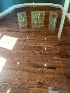 Empty hardwood room with dark wood floors, teal walls, and sunlight from three windows.