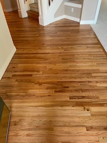 Hardwood floor hallway with white stairs and trim, viewed from an interior entryway.