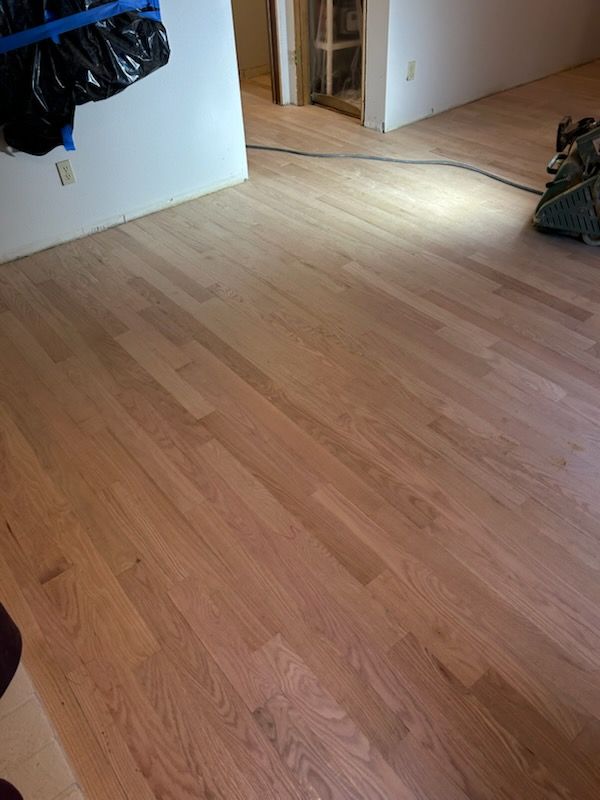 Empty light wood floor in a room with a doorway and a black bag on the left wall.