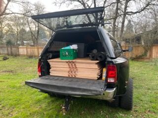 Pickup truck with open tailgate carrying stacked lumber and a green toolbox in a backyard