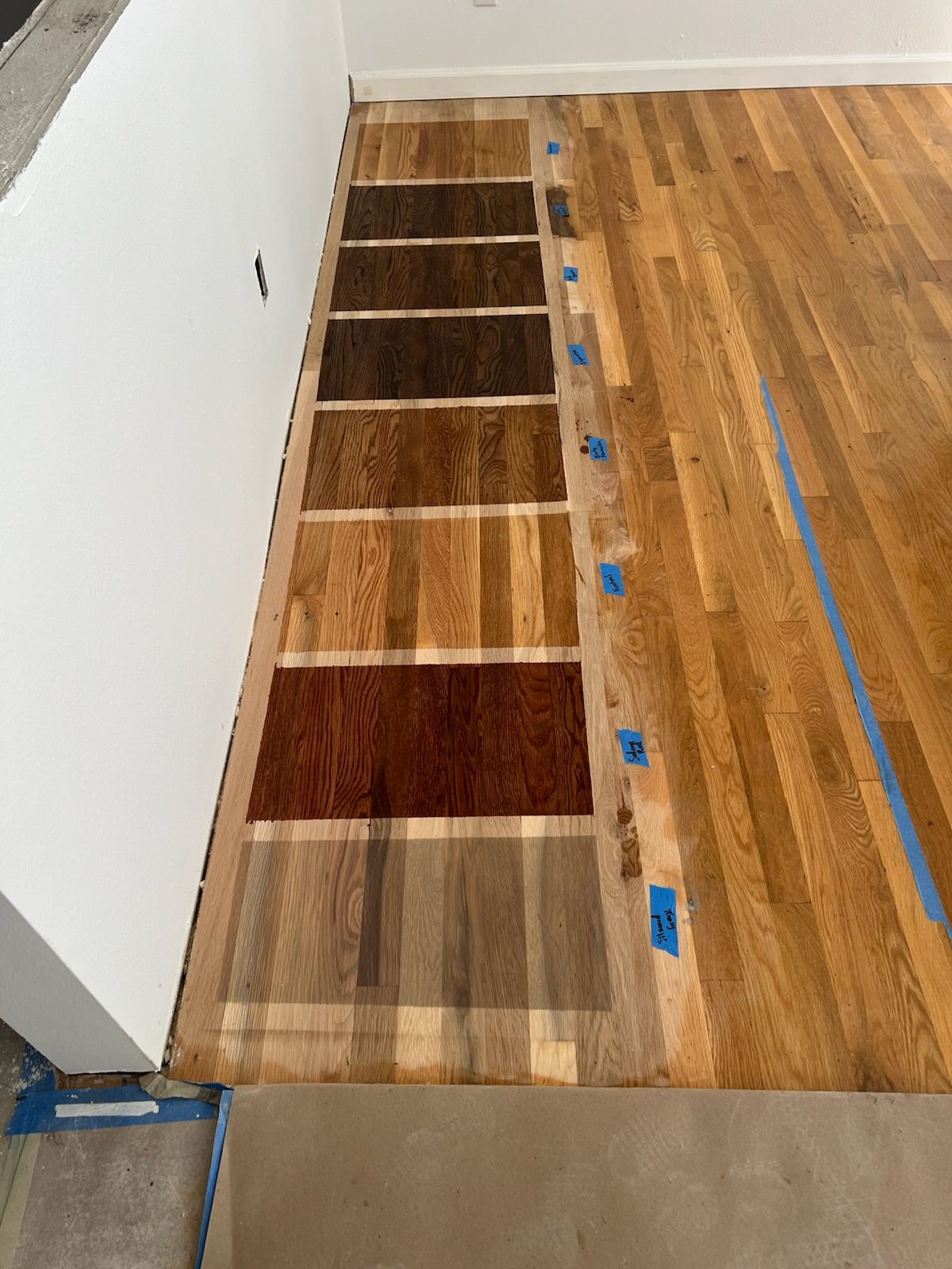 Wood flooring samples laid beside installed hardwood floor, showing color and grain variations