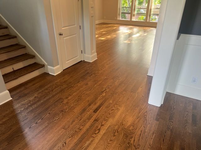 Empty hardwood-floored hallway with stairs and sunlight from windows into an adjacent room