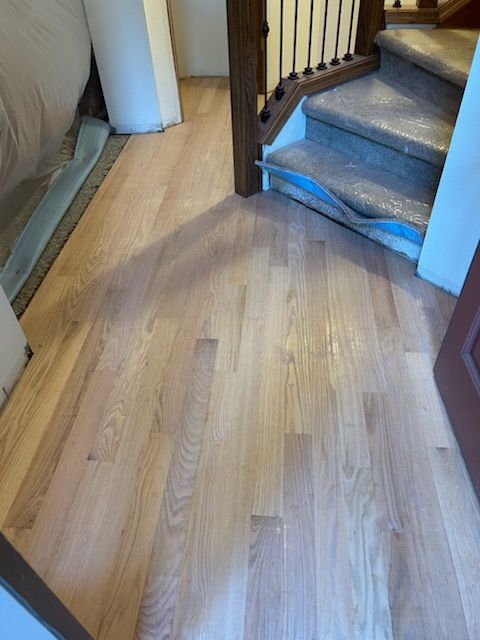 Wooden hallway floor leading to a carpeted staircase with a dark handrail