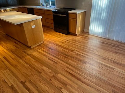 Empty modern kitchen with wood floors, light wood island, and dark cabinetry near a sliding glass door