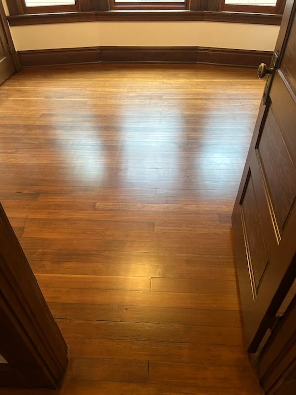 Empty hardwood-floored room with sunlight reflecting from two windows and an open doorway.