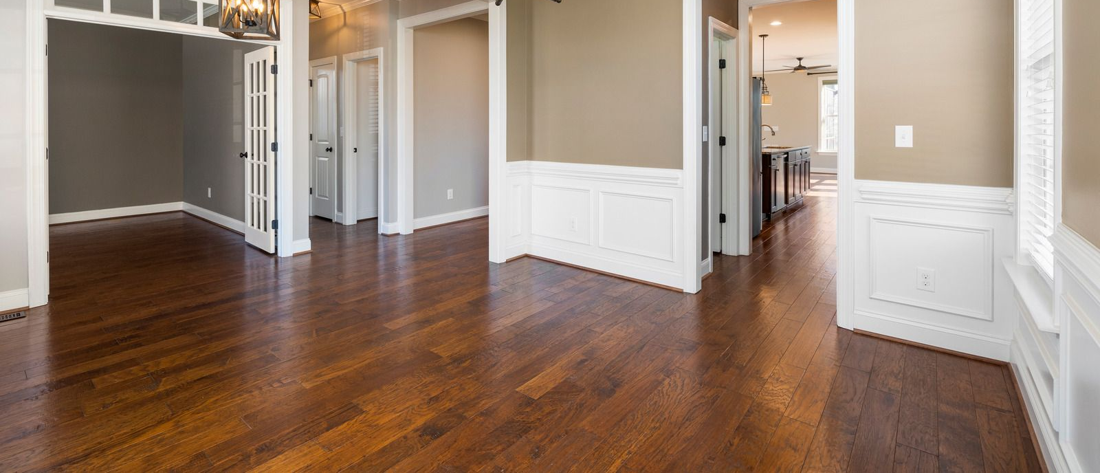 Empty room with dark hardwood floors, beige walls, white trim, and open doorways