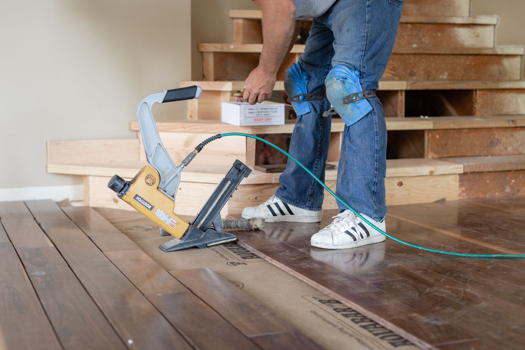 Worker using a nail gun to install hardwood flooring beside stairs