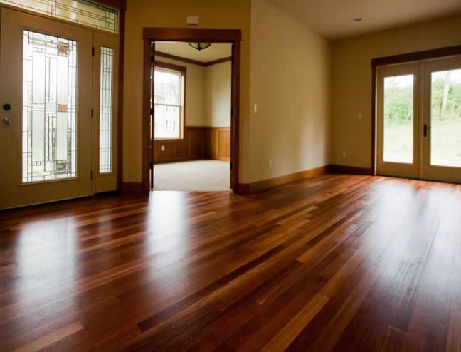 Empty room with polished hardwood floors, large windows, and warm beige walls